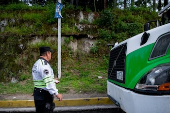 Un gestor de tránsito con uniforme y gorra sostiene un documento frente a la parte frontal de un camión blanco y verde