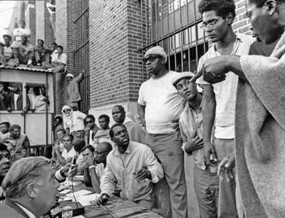 En primer plano, el joven portavoz Elliott James “L.D.” Barkley (con anteojos) y Frank “Big Black” Smith (con gorra blanca, al centro) coordinan las demandas frente a los observadores externos en un intento de frenar la inminente represión armada