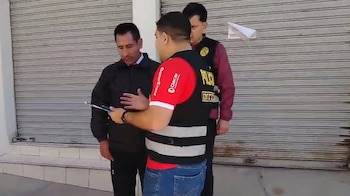 Dos agentes policiales con chalecos informan a un hombre de casaca negra frente a la persiana metálica cerrada de un comercio
