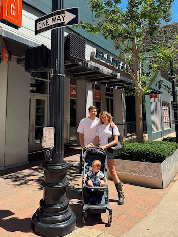 Eva Bargiela y Gianluca Simeone posan en una calle con su bebé Faustino en un cochecito. Detrás, edificios y un poste con una señal de tráfico