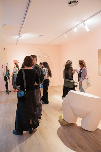 Varias personas observan diversas esculturas y obras de arte en una galería de paredes claras y suelo de madera, con iluminación de riel