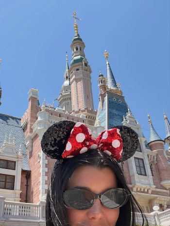 Primer plano de mujer con gafas de sol y orejas de Minnie Mouse con lazo rojo brillante, frente al Castillo de los Sueños Encantados de Disneyland Shanghái