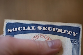 Primer plano de una mano sosteniendo una tarjeta de Seguridad Social azul y blanca con el texto 'SOCIAL SECURITY' visible