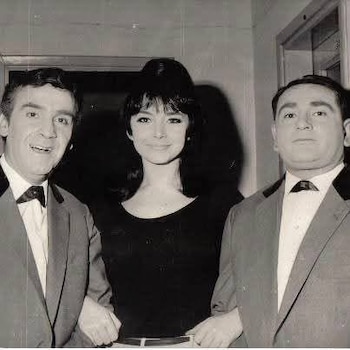 Fotografía en blanco y negro de tres personas. Una mujer de cabello oscuro y flequillo en el centro, flanqueada por dos hombres con traje y corbatín