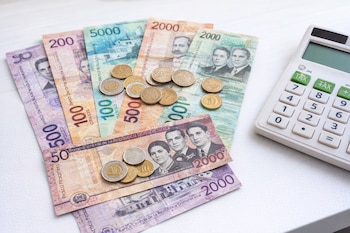 Billetes de varios valores de la República Dominicana, algunas monedas y una calculadora blanca sobre una superficie clara y limpia.