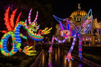 Esculturas de alebrijes luminosos de colores en un camino nocturno con el Palacio de Bellas Artes iluminado al fondo.
