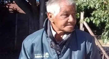 Un hombre mayor, de tez clara y cabello blanco, viste una chaqueta azul oscura y una camisa blanca, mirando ligeramente hacia la derecha del encuadre, con un fondo verde borroso
