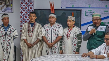 Cinco hombres con vestimenta tradicional indígena y vinchas se encuentran de pie y uno de ellos habla por un micrófono
