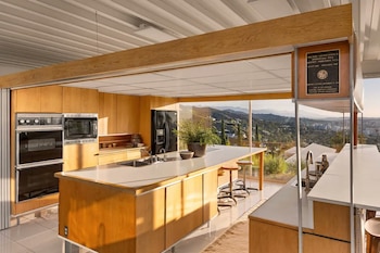 Una cocina con isla central de madera, taburetes, electrodomésticos empotrados y grandes ventanales con vistas a las colinas