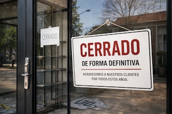 Puerta de cristal con tirador plateado, dos carteles de "Cerrado", uno grande con "Cerrado de forma definitiva" y otro pequeño, interior con estantes vacíos.