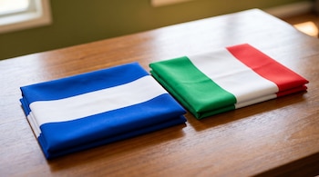 Dos banderas plegadas reposan sobre una mesa de madera. Una bandera es azul y blanca, la otra es verde, blanca y roja.