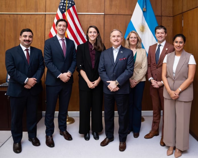 El embajador Peter Lamelas posa con una delegación comercial para promover inversiones frente a las banderas de Estados Unidos y Argentina.