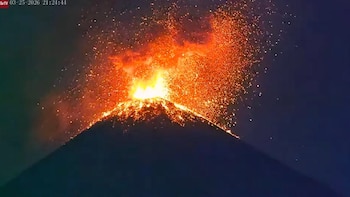 Vista nocturna del Volcán de Fuego en Guatemala, con una explosión de material incandescente y brillante lava fluyendo por sus laderas oscuras