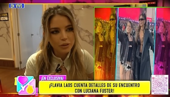 Flavia Laos, rubia y con blusa blanca, siendo entrevistada en primer plano, con recuadros mostrando fotos de ella junto a Luciana Fuster en un evento con público