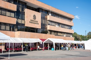Edificio con la inscripción Alcaldía Azcapotzalco y carpas blancas con mesas y personas en una explanada soleada