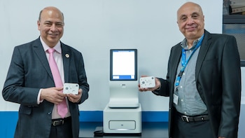 Dos hombres sonrientes en trajes posan con un equipo de biología molecular blanco y pequeños dispositivos portátiles en una sala de fondo claro