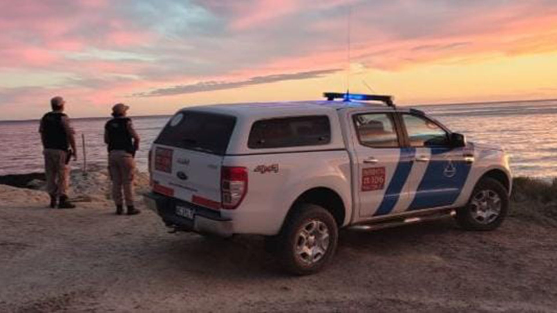 Personal de búsqueda y rescate en la costa de Puerto Madryn durante el atardecer, donde se realiza un operativo para hallar a una mujer desaparecida mientras buceaba.