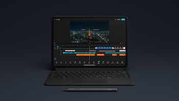 Tableta negra con teclado acoplado y lápiz táctil al frente, con una pantalla que presenta una línea de tiempo de edición de video