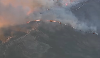 Vista aérea de una línea de fuego y espesas columnas de humo sobre una cresta montañosa en una zona de colinas