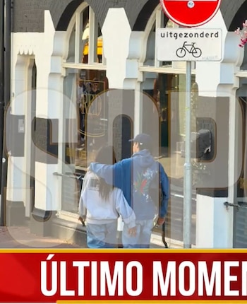 Un hombre y una mujer vistos desde atrás caminan por una acera frente a un comercio y una señal de tráfico