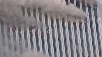 Fachada de un rascacielos con columnas de acero, denso humo gris y varias personas asomadas entre las aberturas de las ventanas