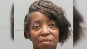 Primer plano de una mujer afroamericana de mediana edad con cabello oscuro y corto, mirando directamente a la cámara con una expresión neutral sobre un fondo gris claro