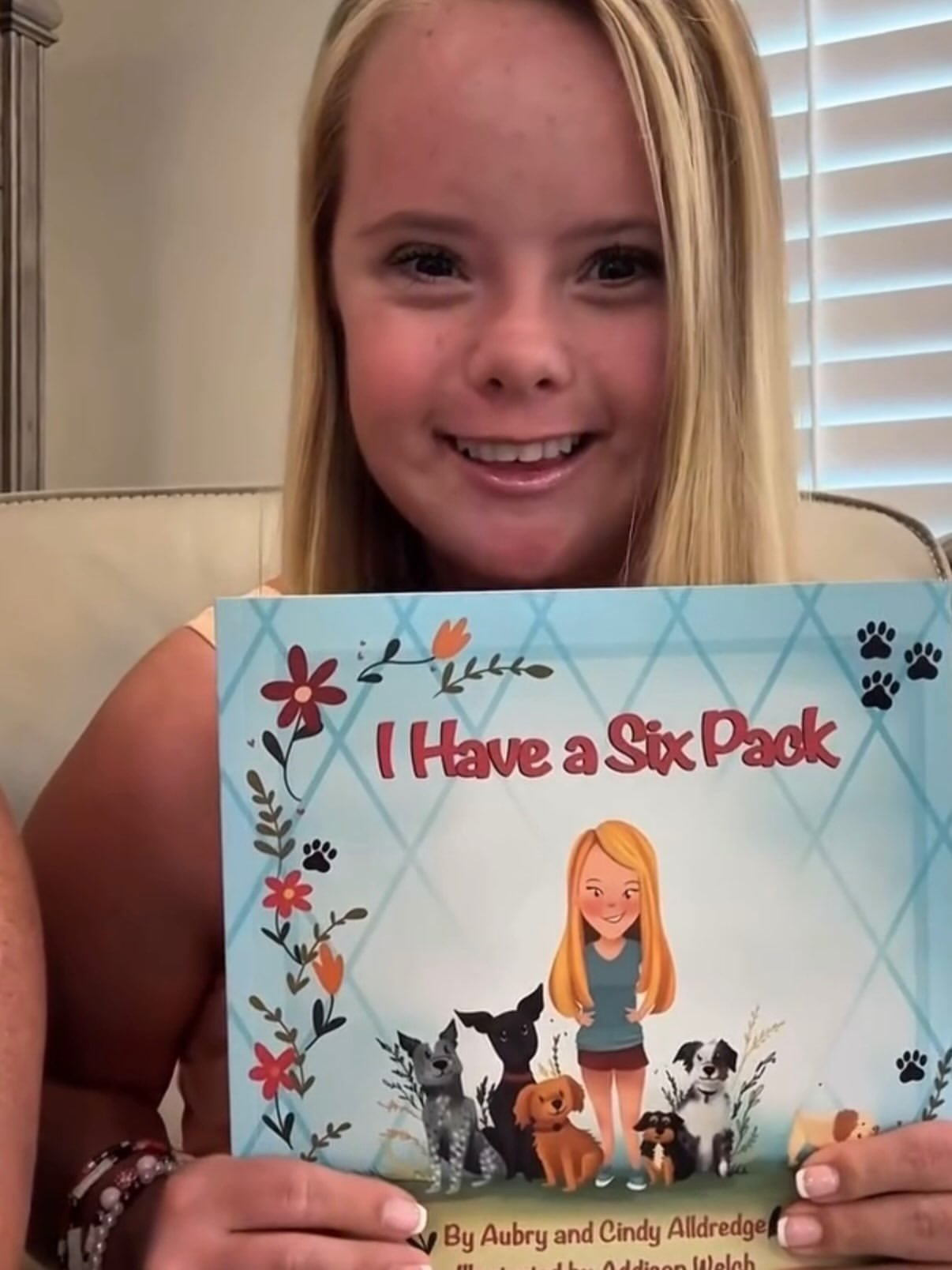 Aubry sostiene la portada de su libro infantil titulado I Have a Six Pack, una obra escrita junto a su hermana que relata las actividades que comparte con sus perros (Ig: @alldredge.aubry)