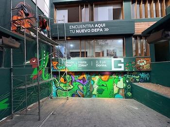 Un edificio con carteles inmobiliarios y murales coloridos, junto a un andamio de metal donde una persona trabaja en una pared
