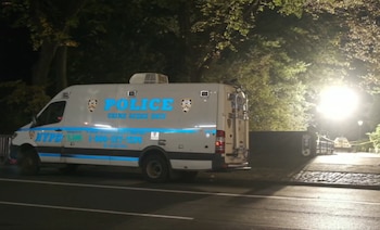 Una furgoneta blanca de la policía con la inscripción Crime Scene Unit está estacionada de noche junto a un sendero iluminado por focos