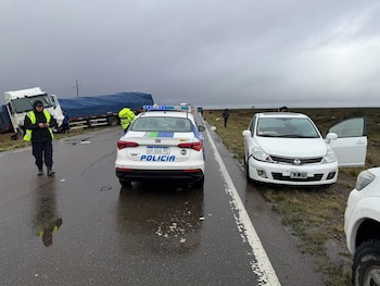 Un camión dañado en la banquina de una ruta mojada, un automóvil blanco detenido a la derecha y personas sobre el asfalto