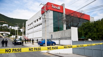 Una cinta plástica amarilla con la frase NO PASE en primer plano frente a un edificio con letrero de Tonalli y policías al fondo.