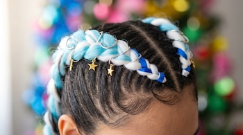 Primer plano de trenzas boxer dobles de kanekalon celeste y blanco decoradas con anillos plateados y pequeños charms de estrella dorados, sobre cabello oscuro.