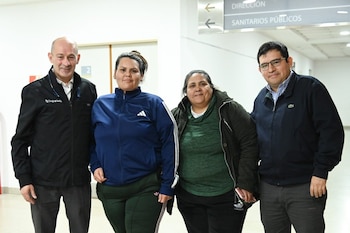 Cuatro personas posan en un pasillo de hospital. Un hombre con chaqueta negra, dos mujeres con ropa deportiva y un hombre con chaqueta oscura y gafas