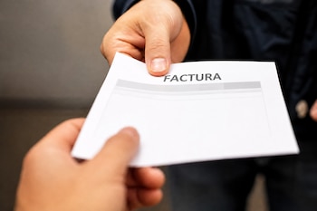 Dos manos sostienen un papel blanco con la palabra FACTURA impresa en letras mayúsculas.