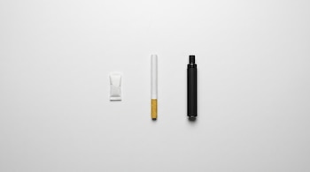 Una bolsita de nicotina, un cigarrillo convencional sin encender y un cigarrillo electrónico negro se alinean sobre una superficie blanca.