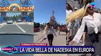 Nadeska Widausky, con cabello rubio y gafas de sol, camina en un parque temático con un castillo de fantasía al fondo, además de una imagen de un coche llegando a una entrada