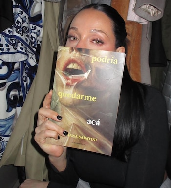 Una mujer de cabello oscuro sostiene el libro 'Podría quedarme acá' de Oriana Sabatini, el cual cubre su boca y nariz, mostrando solo sus ojos