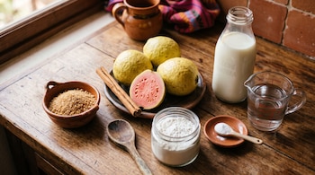 Guayabas, canela, azúcar morena, fécula de maíz, leche, agua y bicarbonato sobre una mesa de madera.