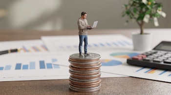 Hombre 3D con sudadera y jeans sobre pila de monedas, usando una laptop. En el fondo, papeles con gráficos, una calculadora y una planta de billetes.