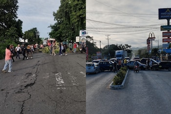 Personas caminan junto a ramas que obstruyen una vía asfaltada mientras varios autos permanecen cruzados e impiden el paso.