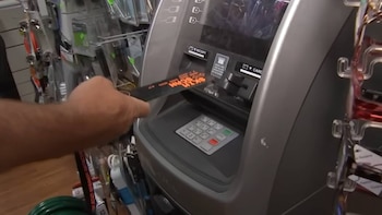 Primer plano de una mano insertando un objeto negro con letras naranjas en la ranura de tarjetas de una máquina electrónica gris con teclado numérico
