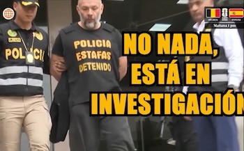 Un hombre calvo con barba, vestido con una camiseta negra que dice "POLICIA ESTAFAS DETENIDO", es escoltado por dos agentes de policía. Hay texto en pantalla