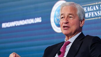 Primer plano de Jamie Dimon hablando, con cabello canoso, traje oscuro y corbata rosa. Al fondo, un letrero azul dice 'REAGANFOUNDATION.ORG'