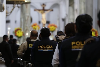 Espaldas de personas, incluyendo agentes con chalecos de 'POLICIA INSPECTORIA GENERAL', dentro de una iglesia con columnas y un crucifijo