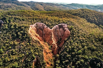 Vista aérea de una hendidura de tierra rojiza en medio de una colina cubierta de árboles densos