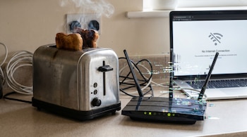 Tostadora con pan humeante junto a un router WiFi con efectos de distorsión y un portátil que muestra 'Sin Conexión a Internet'.