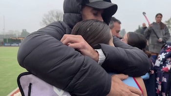 Primer plano de Nicolás Cabré, con gorra y chaqueta oscura, abrazando con cariño a su hija Rufina, quien viste una camiseta azul claro, en una cancha de hockey