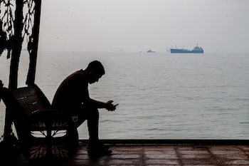 Un hombre mira su celular en un refugio junto a la costa mientras se ven barcos mercantes fondeados, en el estrecho de Ormuz, cerca de Bandar Abbas, Irán, el lunes 6 de octubre de 2026. (Amirhosein Khorgooi/ISNA via AP)