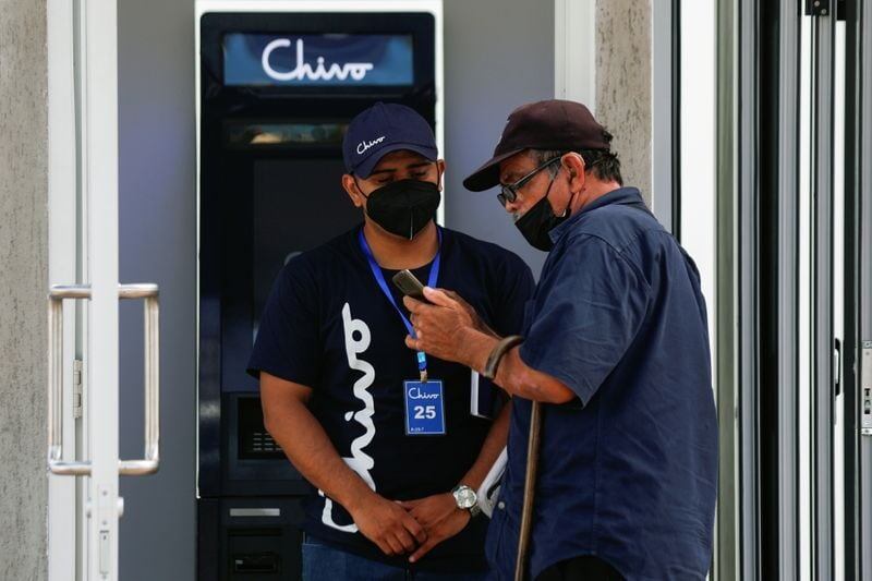 Un trabajador ayuda a un hombre con el uso de bitcoin frente a un cajero automático de
