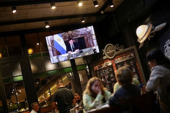 Foto de archivo - Una pantalla muestra al presidente Javier Milei dando un discurso por cadena nacional por televisión, mientras varias personas cenan en un restaurante en Buenos Aires. Abr 22, 2024. REUTERS/Agustin Marcarian